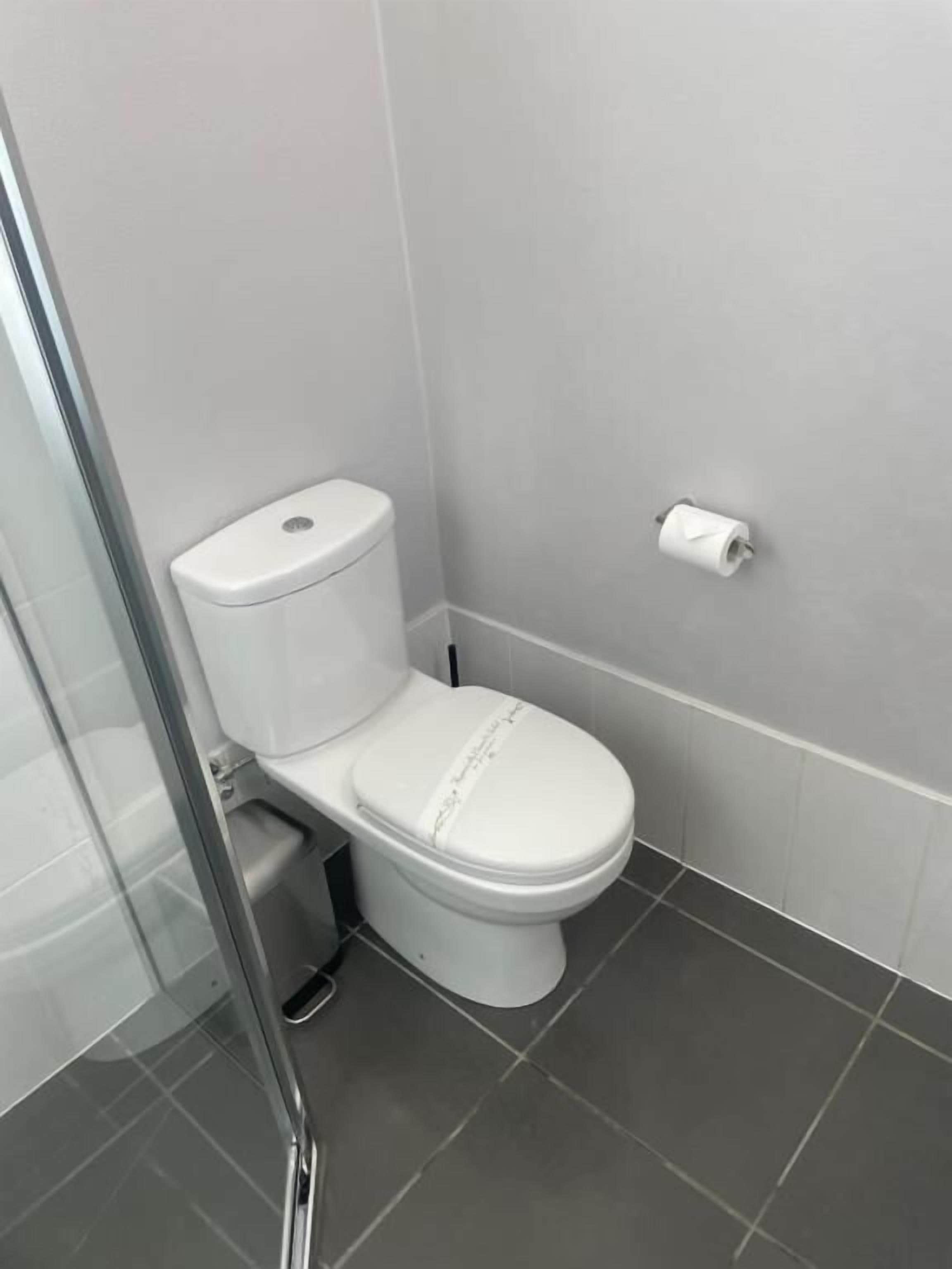 Un baño moderno con inodoro, cabina de ducha de vidrio y un dispensador de papel higiénico en la pared.
