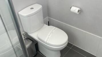 Un baño moderno con inodoro, cabina de ducha de vidrio y un dispensador de papel higiénico en la pared.