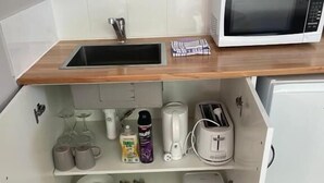 A compact kitchen with a microwave, sink, and storage shelves. - Dawson Motel (Lismore)