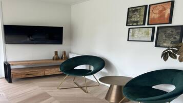 Een moderne woonkamer met een flatscreen televisie, twee groene fauteuils, een ronde salontafel en een bank.