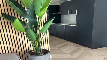 A modern kitchen with dark cabinets, a marble countertop, and a large potted plant.