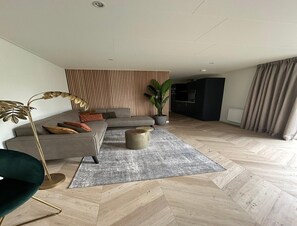 A modern living room with a sofa, a floor lamp, a potted plant, and a herringbone-patterned floor. - Palette Resort De-steppe Family Stay (Ulicoten)