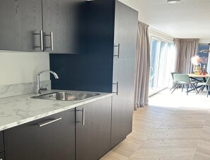 A modern kitchen with dark cabinets, a marble countertop, and a sink. - Palette Resort De-steppe Family Stay (Ulicoten)