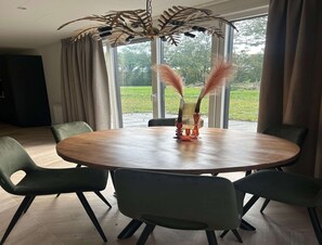 A round wooden table with six green chairs, a decorative vase with feathers, and a ceiling light fixture. - Palette Resort De-steppe Family Stay (Ulicoten)