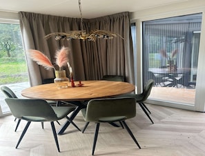 A dining area with a round wooden table, four green chairs, a chandelier, and a view of a patio through large windows. - Palette Resort De-steppe Family Stay (Ulicoten)