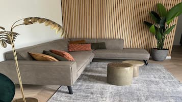 A modern living room with a sectional sofa, a floor lamp, a coffee table, and a large potted plant.