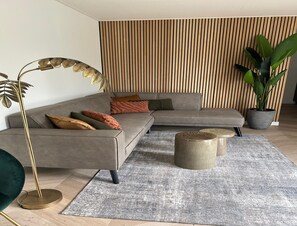 A modern living room with a sectional sofa, a floor lamp, a coffee table, and a large potted plant. - Palette Resort De-steppe Family Stay (Ulicoten)