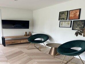 A modern living room with a flat-screen TV, two green chairs, a round coffee table, and a bench. - Palette Resort De-steppe Family Stay (Ulicoten)