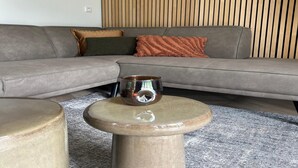 A modern living room with a grey sectional sofa, a round wooden coffee table, and a textured rug. - Eco Forest Home by Palette Resort De-steppe (Ulicoten)