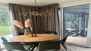 A modern dining area with a round wooden table, four green chairs, a decorative vase with pampas grass, and a unique chandelier. - Family Retreat by Palette Resort De-steppe (Ulicoten)