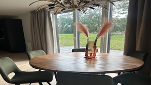 A dining area with a round wooden table, six chairs, and a decorative centerpiece. - Family Retreat by Palette Resort De-steppe (Ulicoten)