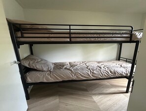 Ein Etagenbett mit Matratze und Kissen, ein Holzboden und eine weiße Tür.