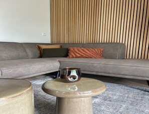 Un salon moderne avec un canapé d’angle gris, une table basse ronde en bois et un tapis gris à motifs.