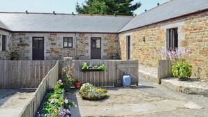 A stone building with multiple doors and windows, surrounded by a wooden fence and potted plants. - Little Content Farm Cottage (Gunwalloe, near Helston)