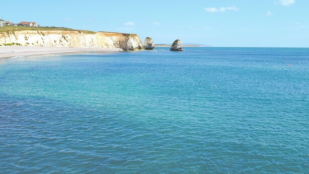 Eine Küstenlandschaft mit klarem Wasser, einem Sandstrand und Felsenformationen.