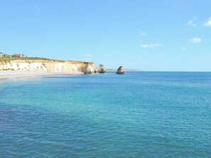 A coastal scene with clear water, a sandy beach, and rocky outcrops. - Old Coastguard Cottage (Freshwater)