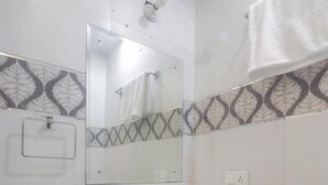 A bathroom with a white sink, a mirror, and a towel hanging on the wall. - HOTEL GRACE (New Delhi)