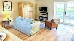 A living room with a sofa, armchair, wooden cabinet, bookshelf, and a television. - Fern Tree Cottage - UK50962 (Kirklington near, Bedale)