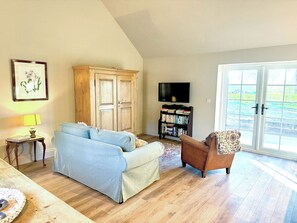 A living room with a sofa, armchair, wooden cabinet, bookshelf, and a television. - Fern Tree Cottage - UK50962 (Kirklington near, Bedale)