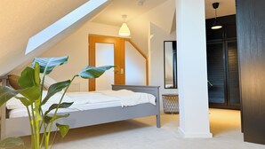 A bedroom with a sloped ceiling, a bed, a potted plant, a bedside table, a mirror, and a wardrobe. - Maisonette apartment, large groups, central - NEW (Erfurt)