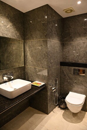 A modern bathroom with a large white sink, a handheld showerhead, and a toilet. - Hotel Sahil Suites (Katra)