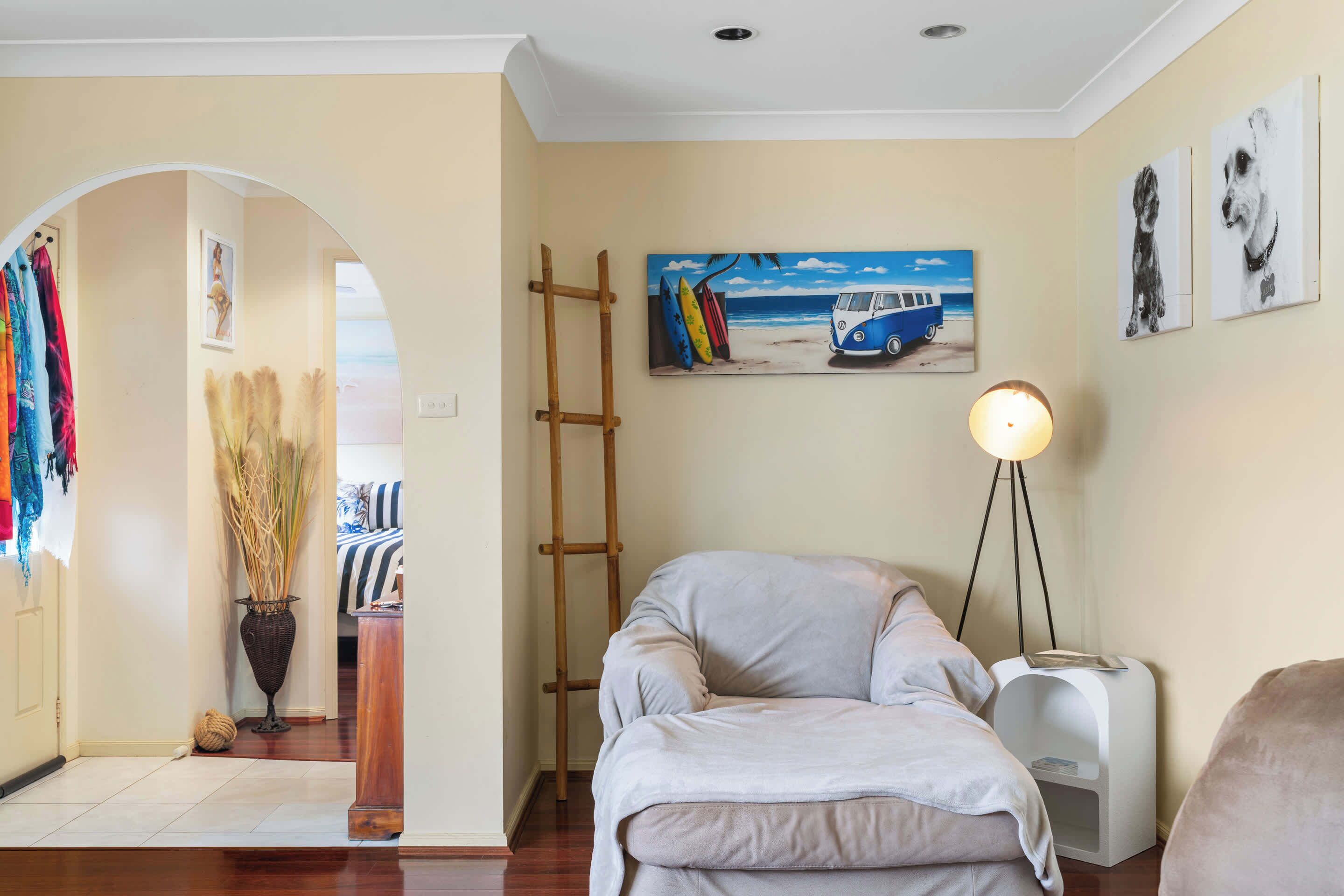 A room with a bed, a lamp, a painting of a beach scene, and a ladder.