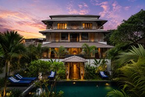 A multi-story hotel with a swimming pool, outdoor seating, and lush greenery.