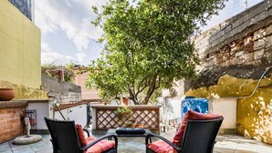 Eine Terrasse im Freien mit zwei Korbstühlen und einem Tisch, umgeben von einer Backsteinmauer und einem Baum.