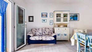 Ein gemütliches Zimmer mit einem blauen Sofa, einer weißen Kommode mit Glastüren und einem Esstisch mit Stühlen.