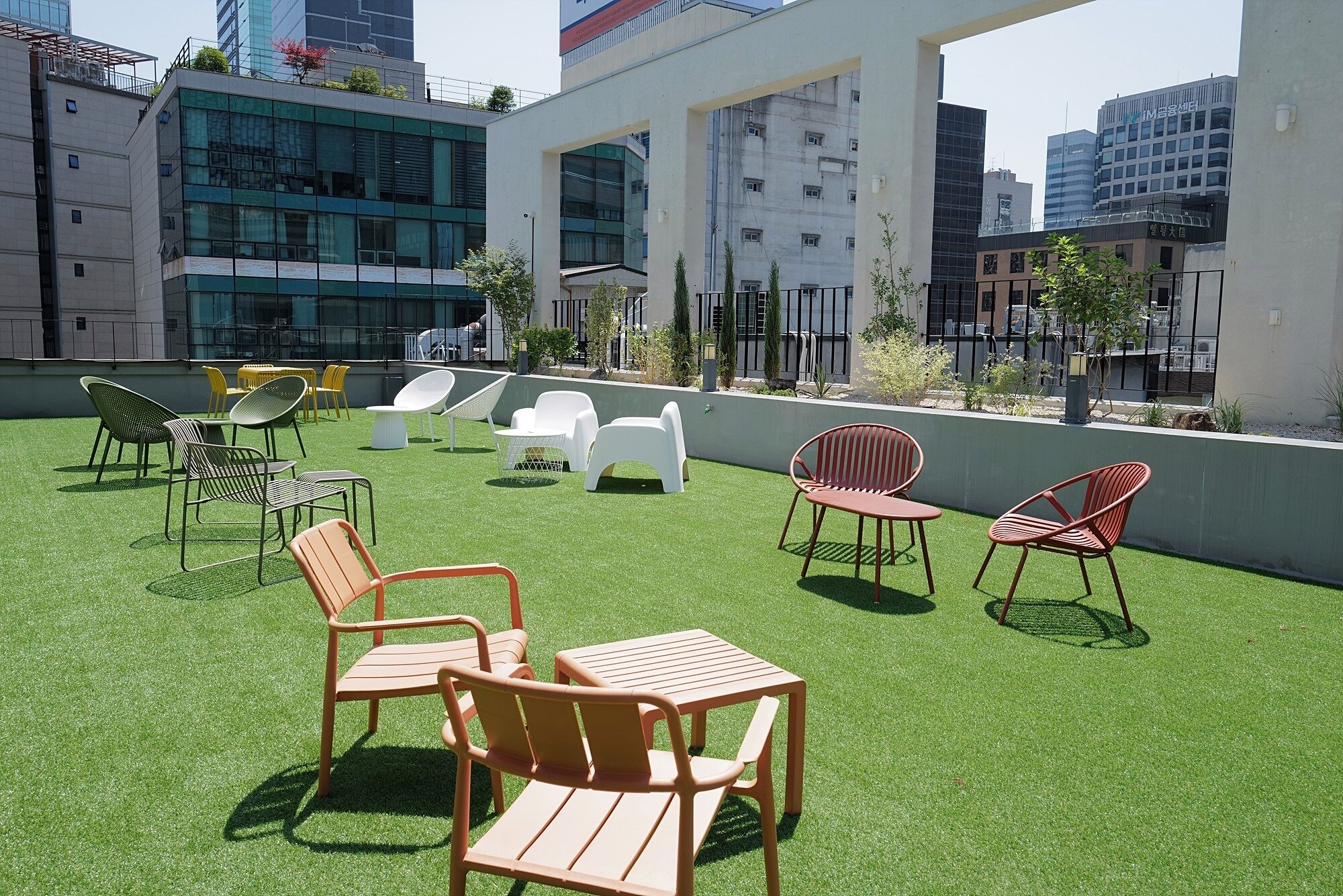 A rooftop terrace with artificial grass, outdoor seating, and modern buildings in the background.