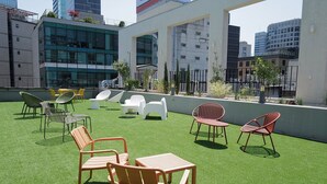 A rooftop terrace with artificial grass, outdoor seating, and modern buildings in the background. - STAY OHANA (Seoul)