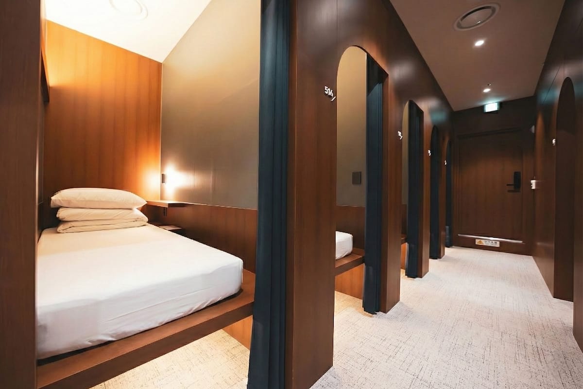 Una camera d'albergo con un letto, pareti in legno e un corridoio con porte.