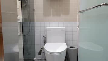 A modern bathroom with a toilet, a glass shower enclosure, and a trash bin.
