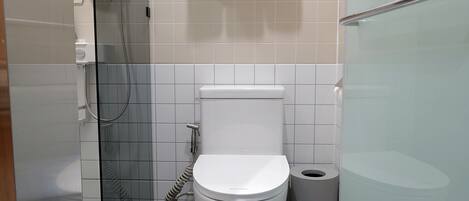 A modern bathroom with a toilet, a glass shower enclosure, and a trash bin.