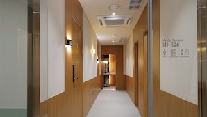 A hotel corridor with wooden paneling, a white carpet, and a sign indicating the Men's Capsule room number 511-526. - STAY OHANA (Seoul)