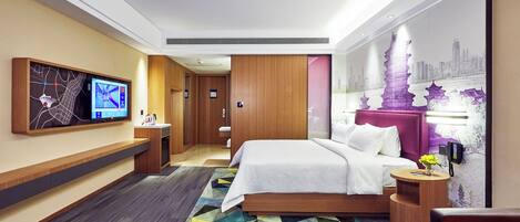 Une chambre d’hôtel moderne dotée d’un grand lit, d’un bureau, d’un téléviseur à écran plat fixé au mur et d’une fresque représentant un paysage urbain.