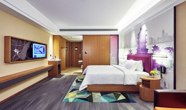 Une chambre d’hôtel moderne dotée d’un grand lit, d’un bureau, d’un téléviseur à écran plat fixé au mur et d’une fresque représentant un paysage urbain.