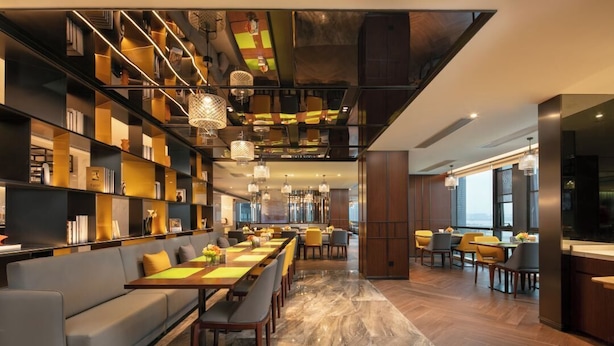 Un hall d’hôtel moderne avec une longue table à manger, des canapés et une bibliothèque remplie de livres.