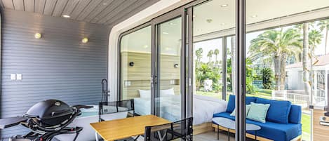 Een moderne buitenruimte met een houten tafel, stoelen, een barbecue en een bank met kussens.