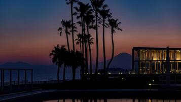 Un resort costero con piscina, palmeras y un edificio moderno con ventanas amplias.