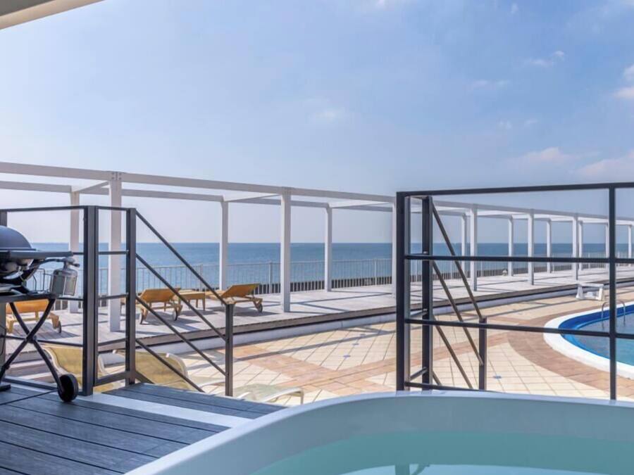 A pool area with a hot tub, lounge chairs, and a view of the sea.