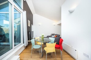 Ein modernes Wohnzimmer mit einem Glastisch, bunten Stühlen, einer Couch und einem großen Fenster.