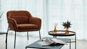 Een moderne woonkamer met een bruine leren fauteuil, een ronde salontafel met een boek en een klein bijzettafeltje met decoratieve objecten.