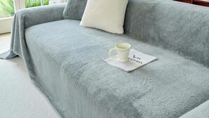 Een gezellige woonkamer met een grijze bank, een witte mok op een onderzetter en een raam met uitzicht op groen.