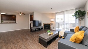 A modern living room with a flat-screen TV, a fireplace, a sofa, and a balcony with a plant. - Spacious 2BR +Rooftop Pool+ view of Hollywood Sign (Los Angeles)