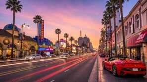 A busy street with palm trees, a red sports car, and illuminated signs, including 'Hollywood' and 'Hollywoodland.' - Spacious 2BR +Rooftop Pool+ view of Hollywood Sign (Los Angeles)