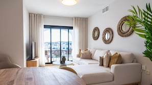 Habitación de hotel moderna con una cama grande, un sofá y un balcón con vistas a la ciudad.