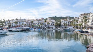 Un puerto deportivo con barcos amarrados, rodeado de edificios blancos con balcones y palmeras.