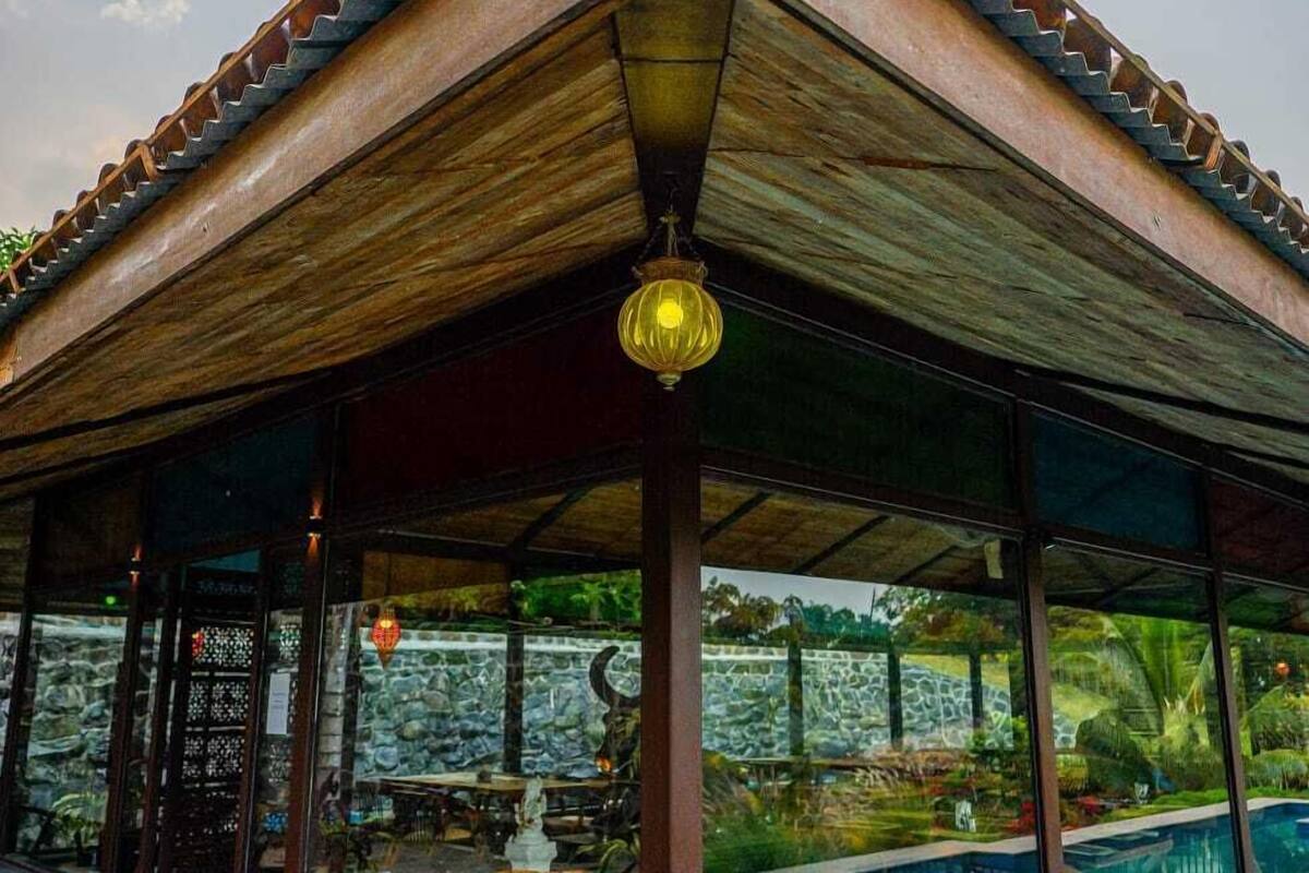 A covered pool area with a wooden roof and stone walls, surrounded by a pool and outdoor seating.