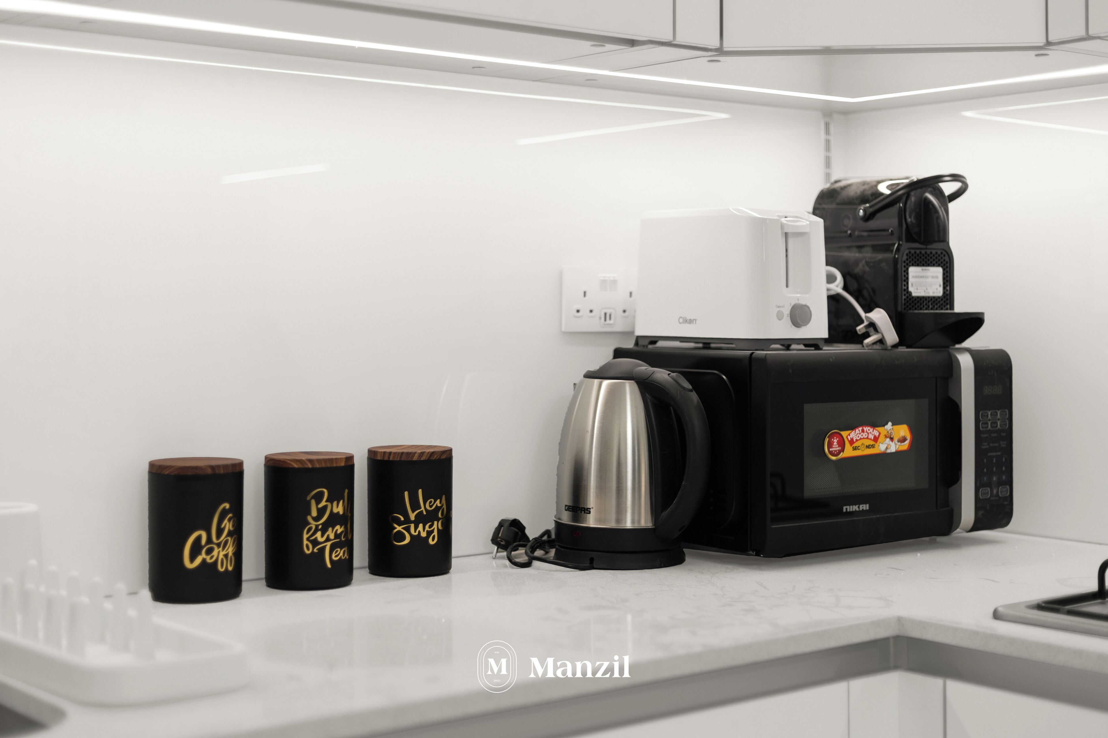 A modern kitchen with a coffee maker, a kettle, and two containers labeled "Coffee" and "Tea".
